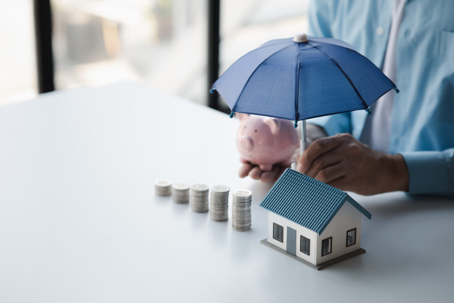 Stacks of coins with a model house and a person holding an umbrella and a piggy bank